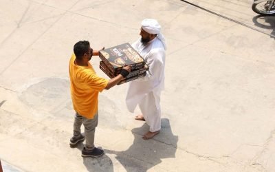 Man in white distributing food packages to a boy in yellow.
