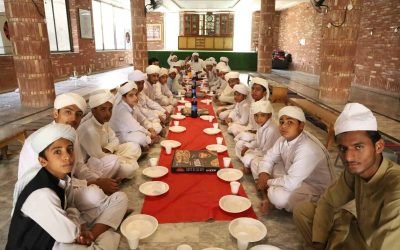 Group of children and adults in traditional attire sitting around a long table.