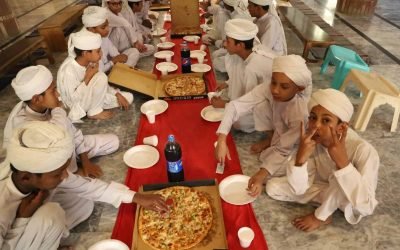 Children in traditional attire enjoying pizza at a community event.