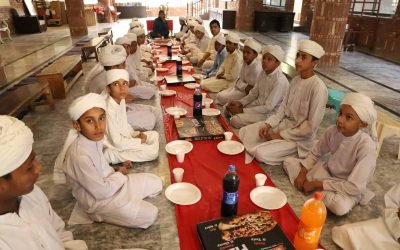 Children in traditional attire sitting at a long table for a meal.